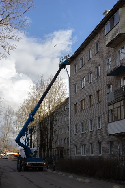 A tall, multi-storey building with external metal staircases on each level, featuring black treads and white railings, situated on a grey facade with several windows and air conditioning units. The st